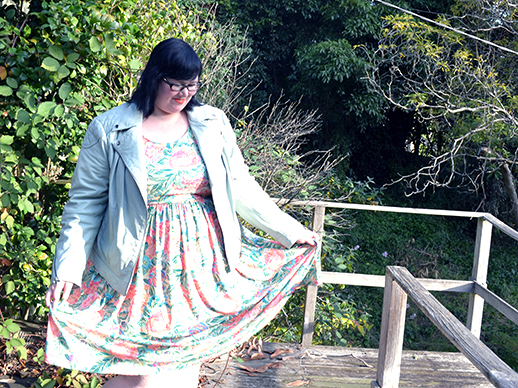 An old and slightly overexposed photo of me with short black hair.  I'm standing outside in a leafy environment, wearing an orange and green floral dress and a mint green leather jacket, smiling down at the skirt I am holding out to either side.  I'm wearing glasses and orange lipstick too.